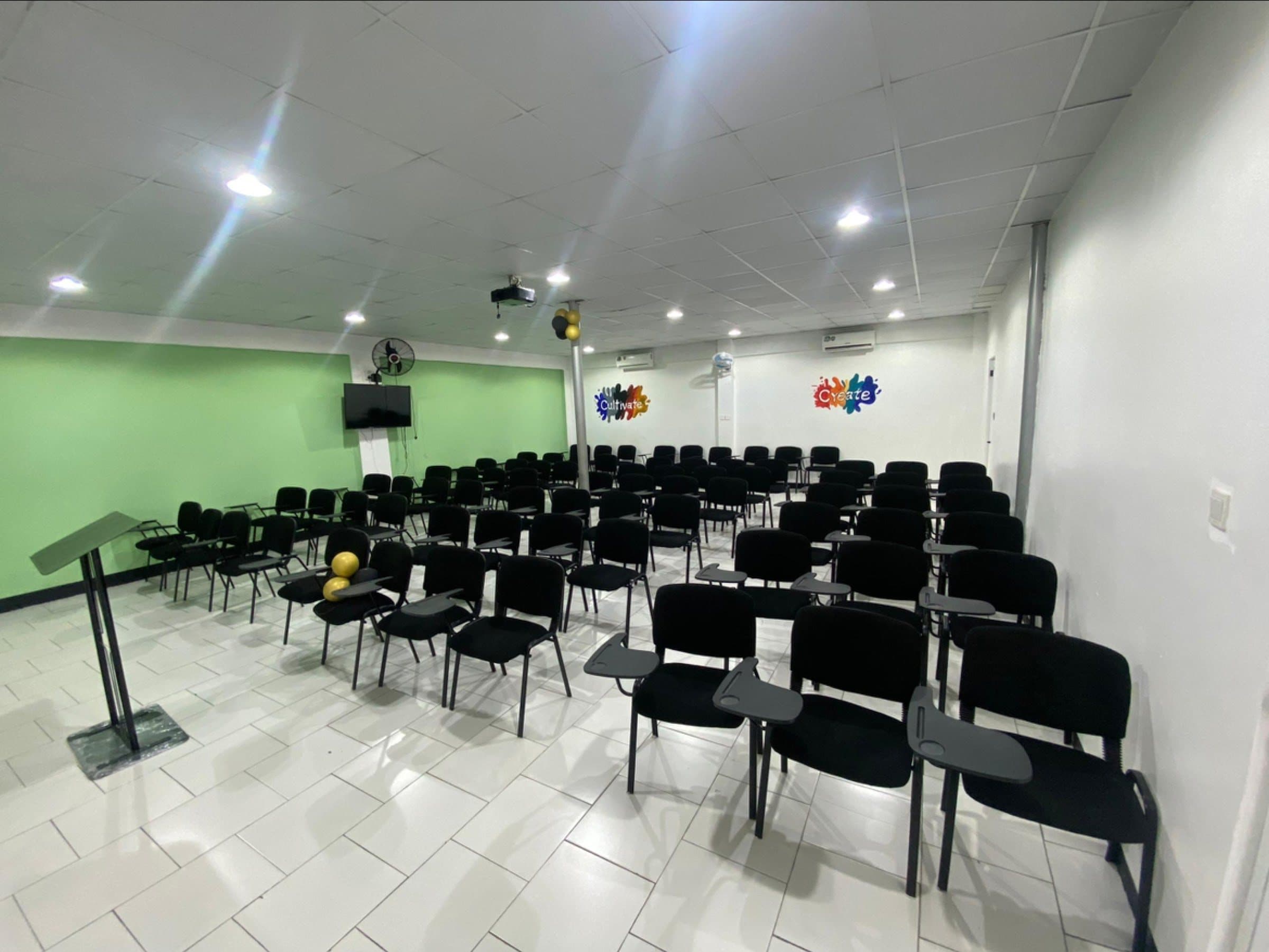 Cr8tivebox conference room with rows of black seats, a lectern, projector and green feature wall