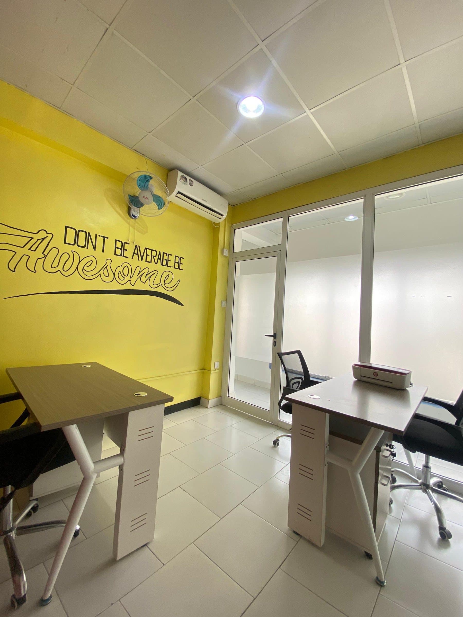 Executive office at Cr8tivebox with two desks, glass partition and a yellow feature wall reading “Don’t be average, be awesome”